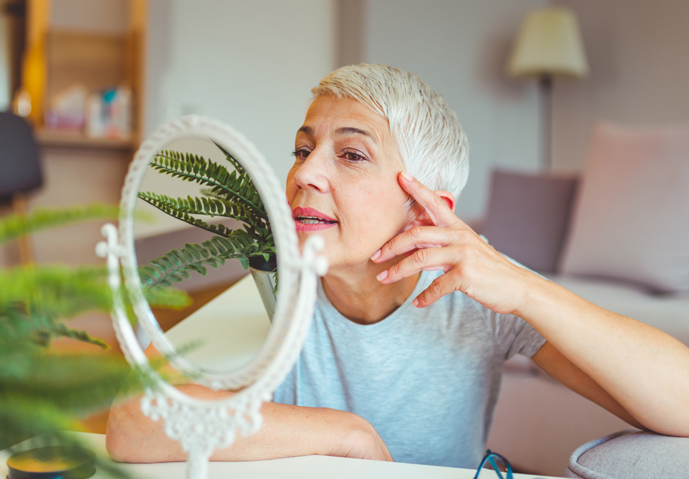 An elderly woman looks into a mirror.